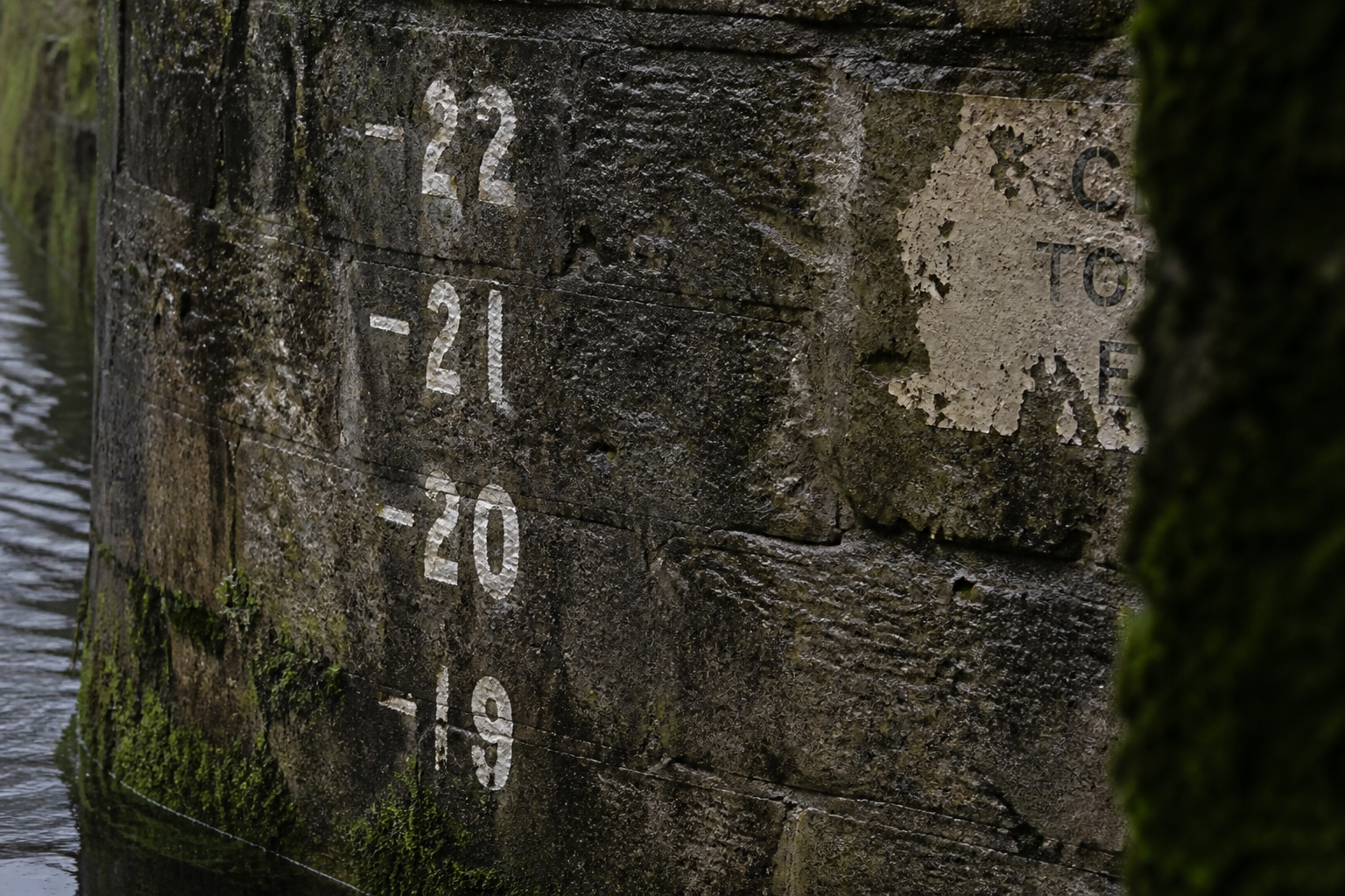 Painted depth marker numerals on wet grey lock-chamber stone